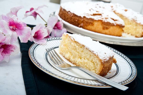 One plate with a slice of an apple cake with the big cake on the background. Flowers like freshness of the cake.