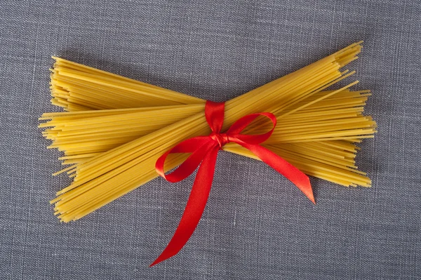 Bando de espaguete com uma fita vermelha em uma toalha de mesa pronta para ser cozida em uma receita italiana — Fotografia de Stock