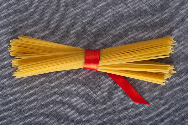 Bando de espaguete com uma fita vermelha em uma toalha de mesa pronta para ser cozida em uma receita italiana — Fotografia de Stock