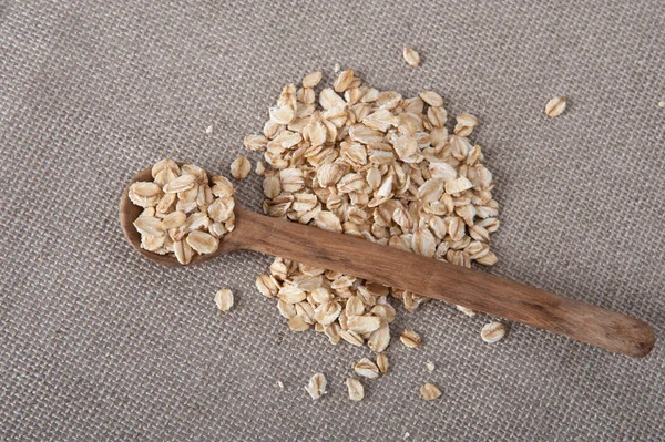 Pile of oat on a beige table cloth with a wooden spoon — Stock Photo, Image