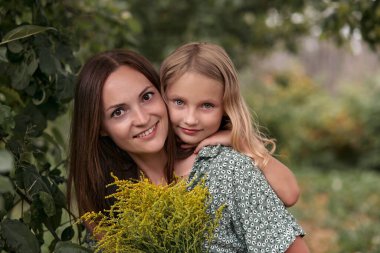 Güzel, genç bir anne, küçük sevimli bir kıza sarılıyor.