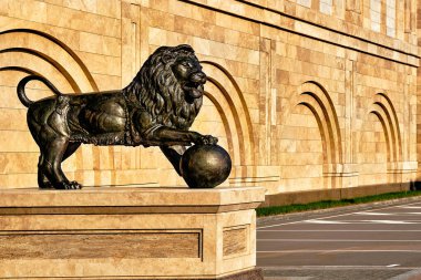 Sarı-kahverengi görkemli bir binanın arka planında bronz bir aslan heykeli