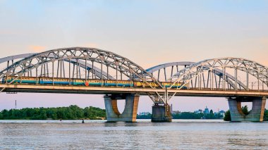 Nehrin karşısındaki demiryolu köprüsünden bir yolcu treni geçiyor.
