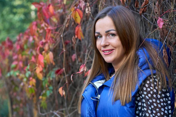 Cute smiling girl in a blue vest and red orange bushes — стоковое фото