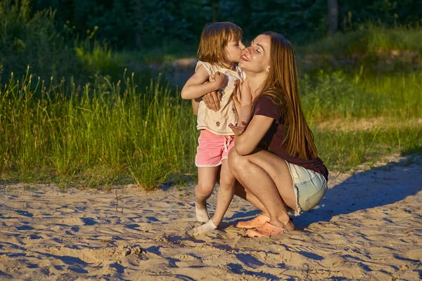 Прекрасная милая девочка целует счастливую маму среди песчаных дюн и зелени — стоковое фото
