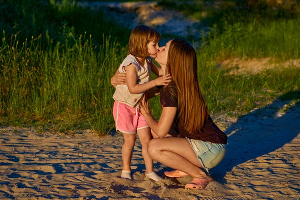 Прекрасная милая девочка целует счастливую маму среди песчаных дюн и зелени — стоковое фото