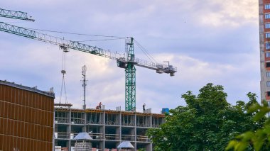 a large, tall machine used for moving heavy objects by suspending them from a projecting arm or beam. Construction high crane,building and blue cloud sky