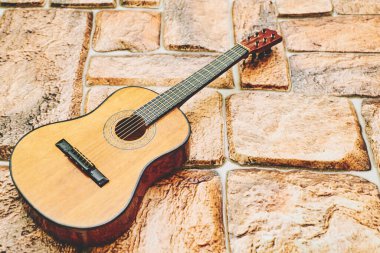Bir telli müzik enstrümanı, üzerinde de keçeli bir klavye var. Turuncu tuğla kaldırım taşı yüzeyinde akustik sarı kahverengi gitar.. 