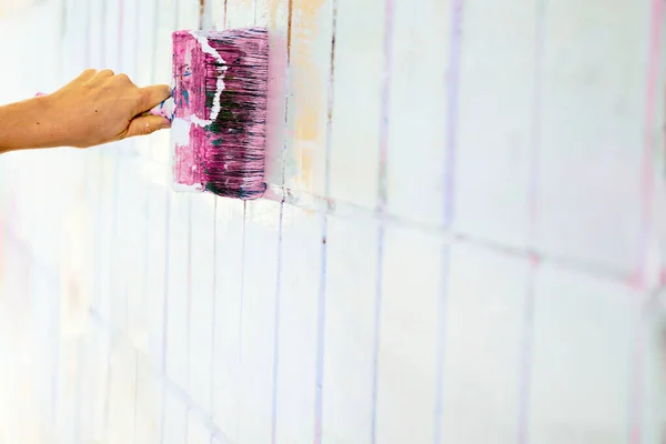 the process or skill of applying a substance to something so as to change its original color. Brush painting dyeing surface of white wall with pink magenta paint