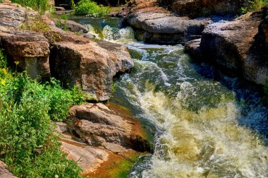 a large natural stream of water flowing in a channel to the sea, a lake, or another such stream. Stormy fast cleaner flow of a mountain river among a stone brown formation.