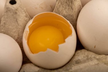 Beyaz tavuk yumurtaları ve beyaz kartondan yapılmış bir tepside kırılmış bir yumurta.