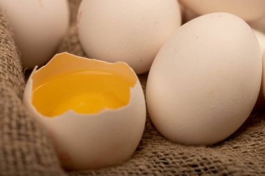 Kırık bir beyaz tavuk yumurtası ve ev yapımı kumaşlı, seçici odaklı, pürüzsüz bir kumaş üzerinde birkaç tam yumurta.