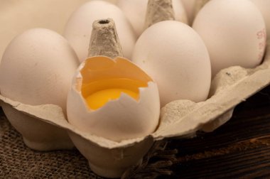 Beyaz tavuk yumurtaları ve beyaz kartondan yapılmış bir tepside kırılmış bir yumurta.