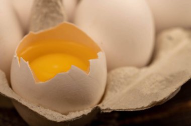 Beyaz tavuk yumurtaları ve beyaz kartondan yapılmış bir tepside kırılmış bir yumurta.