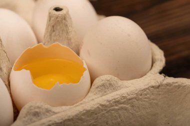 Beyaz tavuk yumurtaları ve beyaz kartondan yapılmış bir tepside kırılmış bir yumurta.