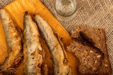 Tahtada küçük bir balık, bir parça ekmek ve bir bardak votka, yakın plan, seçici odaklanma.