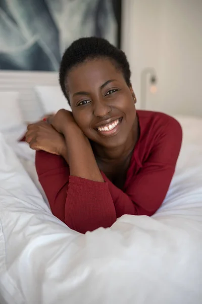 Close up portrait of beautiful Black African woman laying on bed with legs and arms crossed, smiling and looking into the camera