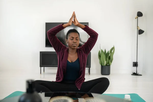 Close up of black African woman sitting in yoga pose on mat in living room, Stretching and meditation at home work out