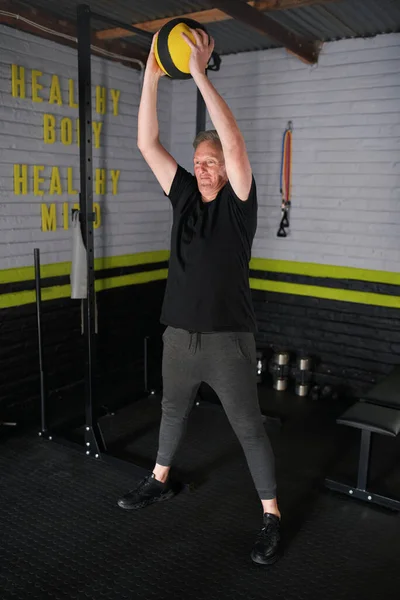 Mature man exercising in home garage gym. Senior man doing weighted medicine ball smashes exercise.