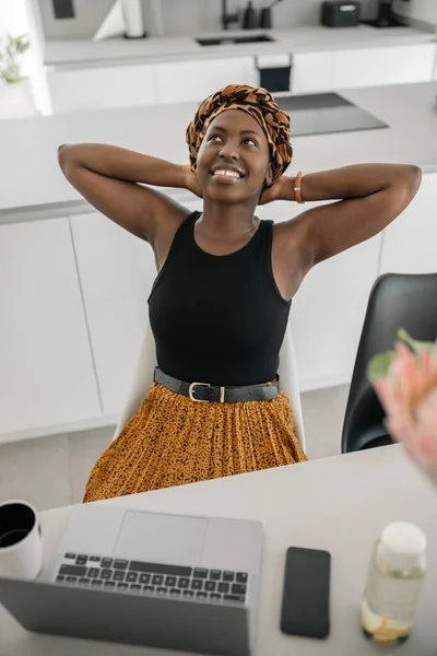 Black African traditional business woman working from home. Looking up, stretching and arms behind her day dreaming, wearing inspired head scarf