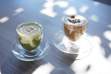 Kahve dükkanında şeffaf bardakta sıcak yeşil çay ve kahve çok güzel ışıklandırılmış. Sütlü kafe içeceği..