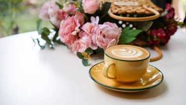 Kahve dükkanında beyaz seramik bardağın üzerinde lale sütlü latte ile Latte sanat kahvesi beyaz köpüklü sıcak çikolata içeceği ve kısa bardakta kakao kahverengi toz..