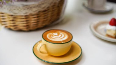 Kahve dükkanında beyaz seramik bardağın üzerinde lale sütlü latte ile Latte sanat kahvesi beyaz köpüklü sıcak çikolata içeceği ve kısa bardakta kakao kahverengi toz..