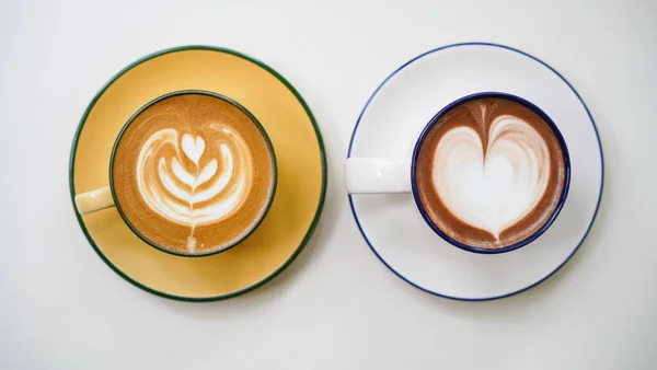 Latte art hot coffee with tulip milk latte art on top of white ceramic glass set on table in coffee shop Hot chocolate drink with white foam and cacao brown powder on top in short cup.