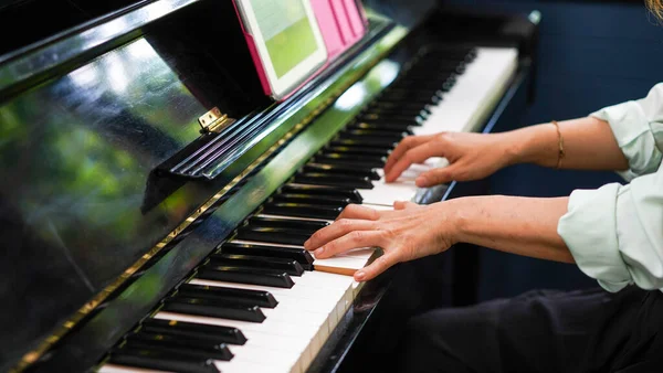 Adult woman plays electronic piano with note sheet. Professional pianist showing solo on acoustic black piano. practicing and learning how to play song. Classic instrument.