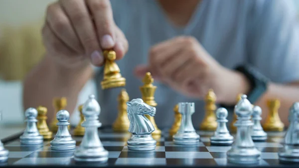 Chess is board game to improve thinking and strategy planning. Gold and silver chess on board in room for playing. Hand holds chess.