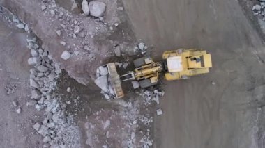Havadan bakan tekerlek yükleyicisi tırtıl taş ocağına çakıl taşı atıyor. Taşlar uçurumdan yuvarlanıyor..