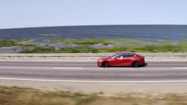 Kırmızı Tesla Model 3 körfez boyunca yolda ilerliyor. Yüksek kalite 4k görüntü