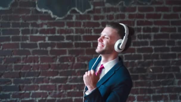 Beau homme d'affaires habillé costume d'affaires casque dansant fond de mur de brique rouge intérieur — Video