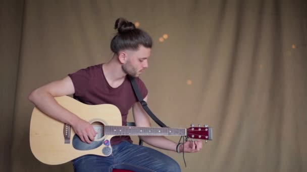 Przystojny młody człowiek gra gitara akustyczna siedzi krzesło tkanina tło — Wideo stockowe