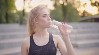 Spor ve Spor. Genç Kafkas Kadın Spor Giyinik Su İçen Plastik Şişe Dışarıda duran Yaz Parkı Güneş Işığı Arkaplanı