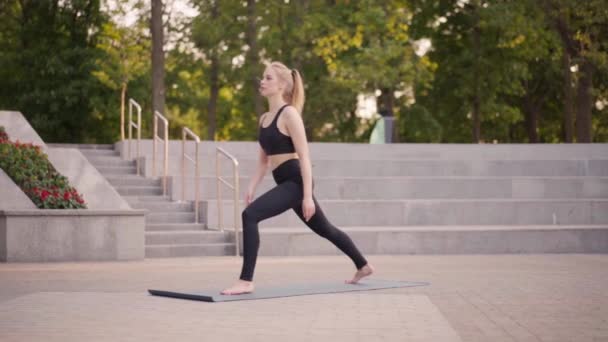 Fitness femme pratique des exercices de yoga sur tapis extérieur ville lumière du soleil arrière-plan — Video
