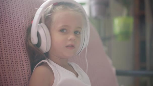 Sofá de niña sentada en auriculares Escuchar música Usar el ordenador portátil Divertirse Inicio Interior Caucásico Femenino Uso del Niño Tecnología Niños modernos Infancia feliz — Vídeo de stock