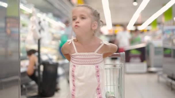 Αστείο χαριτωμένο παιδί πιέζει καλάθι αγορών στο σούπερ μάρκετ — Αρχείο Βίντεο