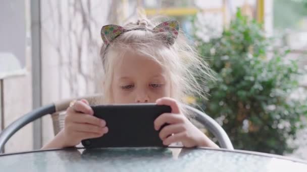 Kislány néz videó okostelefon képernyőn ül szabadtéri kávézó — Stock videók