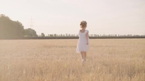 Kislány fut napsütéses nap mezőgazdasági területen öltözött fehér ruha Boldog gyermekkori koncepció — Stock videók