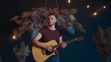 Erkek müzisyen akustik gitar çalarak arkasını döner. Gitarist konserde sahnede klasik gitar çalar.
