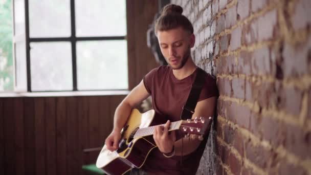 Hombre con guitarra acústica apoyado en la pared de ladrillo tocando música cantando canciones disfrutar de la vida — Vídeo de stock