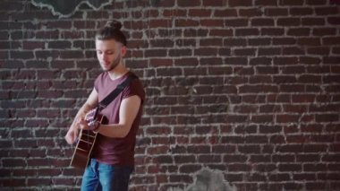 Akustik gitarlı bir adam ileri geri yürür tuğla duvar arkası müzik besteler şarkı söyler, hayatın tadını çıkarır.