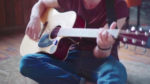 Hezký mladý muž hraje na akustickou kytaru sedí na podlaze obývací podkrovní místnosti — Stock video