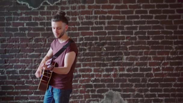 Człowiek z gitarą akustyczną spacery w tę i z powrotem ceglane tło ściany komponuje muzykę gra śpiew piosenki cieszyć się życiem Medium shoot — Wideo stockowe