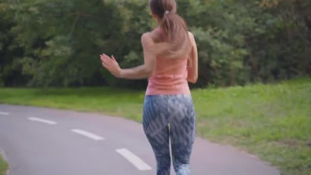 Спортивная женщина бегает беговая дорожка в парке летний день Кавказская женщина бег трусцой одет спортивная одежда Средний стрелять задний вид замедленной съемки — стоковое видео