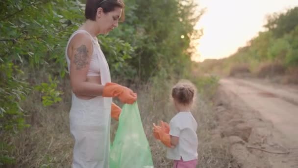 Маленькая девочка помогает матери собирать пластиковый мусор на природе, чтобы спасти окружающую среду от загрязнения — стоковое видео