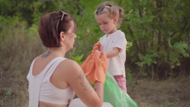 Mała dziewczynka założona rękawiczki, aby pomóc matce zbiera plastikowe śmieci na przyrodę, aby uratować środowisko przed zanieczyszczeniem — Wideo stockowe