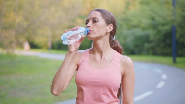 Kvinna löpare dricka vatten transparent plastflaska efter morgonen jogging kaukasiska atletisk hona vilar efter träning sommardag i parken — Stockvideo