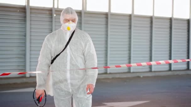 Hombre, trabajador parado línea fronteriza señal de advertencia desinfecta, pulveriza productos químicos en la superficie contra el coronavirus. Medidas sanitarias en lugar público durante la cuarentena — Vídeo de stock